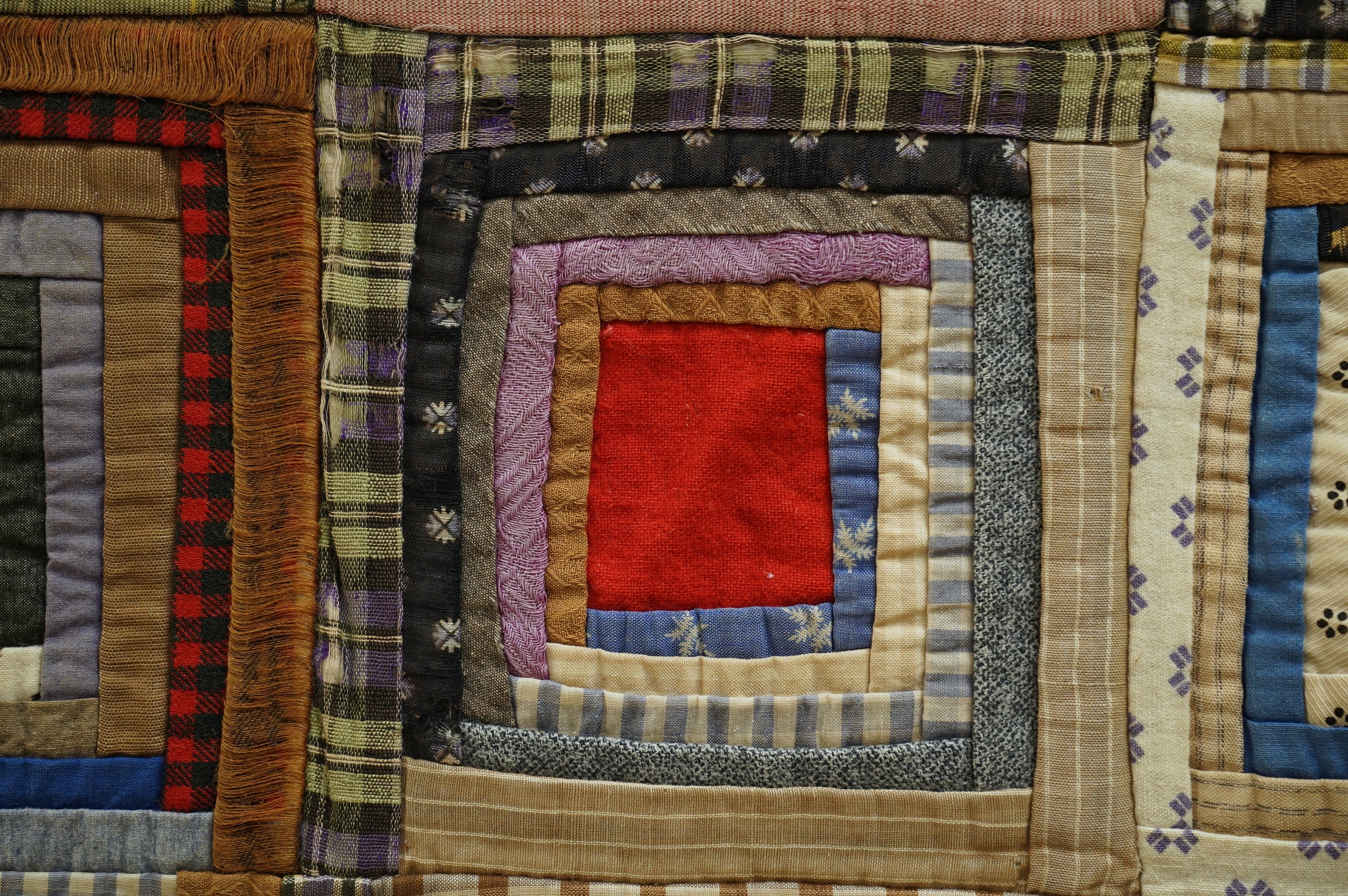 An early 20th century American ‘Log Cabin’ quilt, with a simple same coloured squared patchwork under side, the ‘Log Cabin’ worked in narrow bands of multi patterned and coloured strips of fabric into squares with a plai